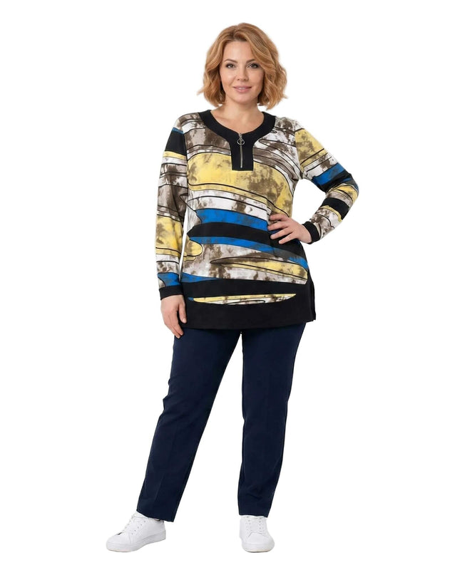 Μακριά εμπριμέ τουνίκ σε μεγάλα μεγέθη με αφηρημένο πολύχρωμο σχέδιο και λειτουργικό φερμουάρ, παρουσιασμένη σε ολόσωμη λήψη φορεμένη με μπλε παντελόνι.