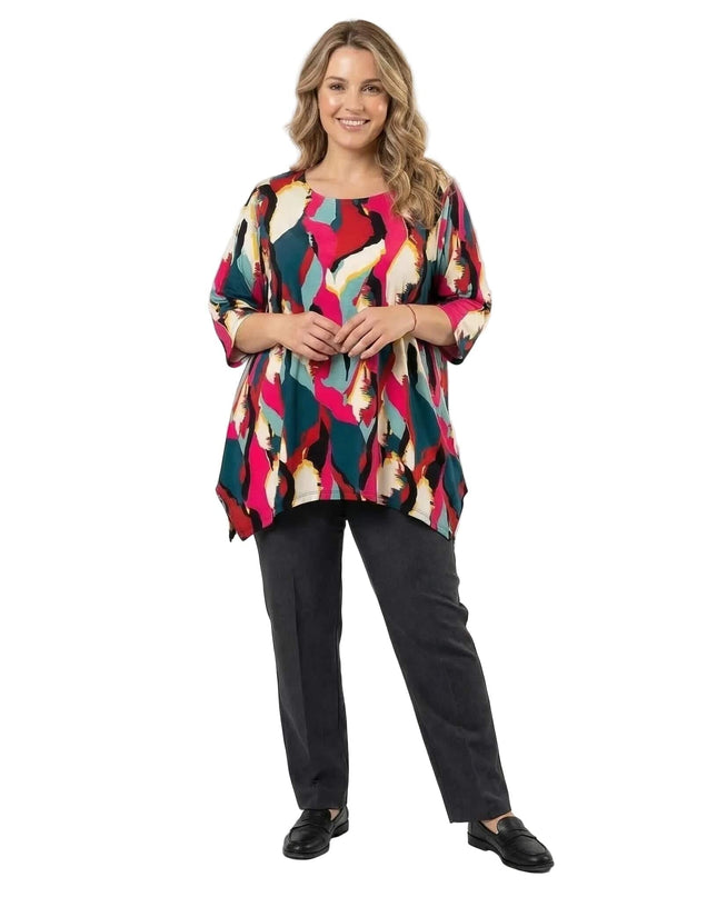 Ολόσωμη λήψη μοντέλου που φοράει μακριά καλοκαιρινή plus size τουνίκ με εντυπωσιακό πολύχρωμο αφηρημένο μοτίβο και σκούρο γκρι παντελόνι.