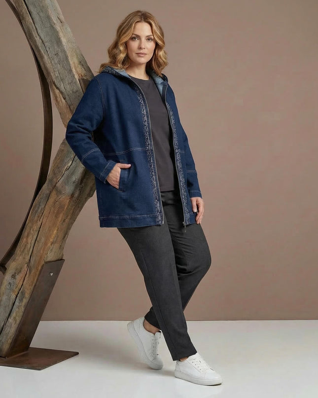 Ολόσωμη λήψη με γυναίκα να φοράει μακρύ σκούρο μπλε τζιν μπουφάν με κουκούλα σε μεγάλα μεγέθη, συνδυασμένο με γκρι ρούχα και λευκά sneakers.