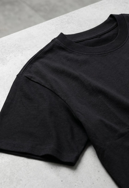 Κοντινή λεπτομέρεια σε flat lay που δείχνει τη στρογγυλή λαιμόκοψη και το μανίκι από τη μαύρη βαμβακερή μπλούζα σε μεγάλα μεγέθη.