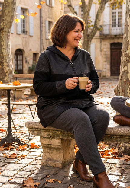 Μαύρη γυναικεία ζακέτα με κουκούλα σε μεγάλα μεγέθη, φορεμένη από γυναίκα που κάθεται σε πέτρινο παγκάκι σε εξωτερικό χώρο.