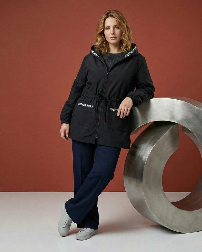 Μαύρο αντιανεμικό μπουφάν σε μεγάλα μεγέθη με κουκούλα και κορδόνι στη μέση, διακοσμημένο με λευκή τυπογραφία στις λεπτομέρειες, σε ολόσωμη λήψη.