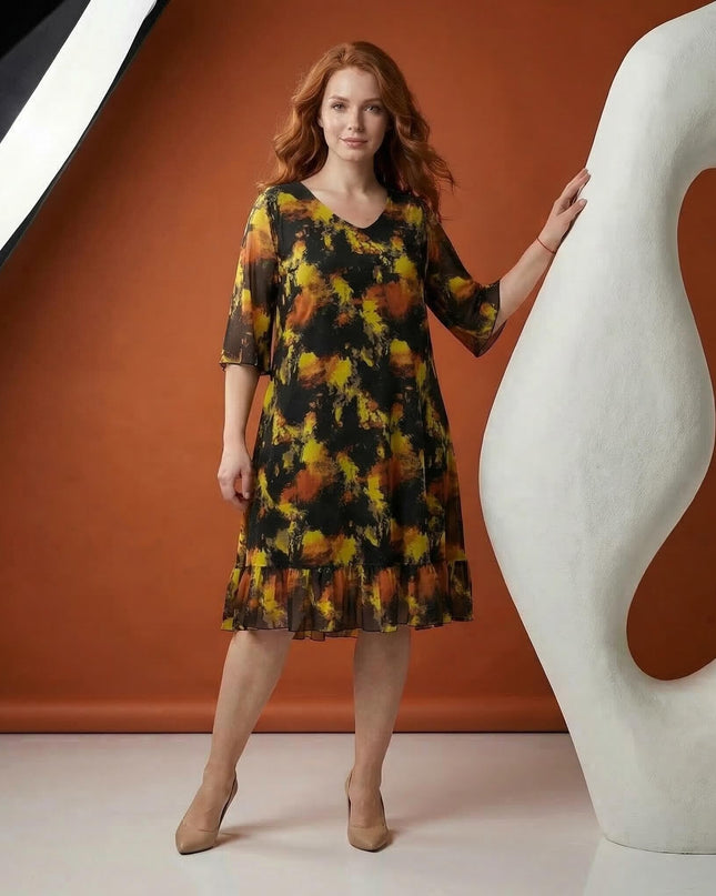 Ολόσωμη λήψη μοντέλου με μαύρο επίσημο γυναικείο σιφόν φόρεμα μεγάλα μεγέθη, το οποίο διαθέτει κίτρινο και πορτοκαλί αφηρημένο μοτίβο και μανίκια καμπάνα.