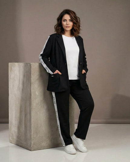 Μαύρο καθημερινό γυναικείο σετ σακάκι και παντελόνι σε μεγάλα μεγέθη, διακοσμημένο με λευκές ρίγες στα πλαϊνά. Ολόσωμη λήψη που παρουσιάζει την άνετη εφαρμογή.