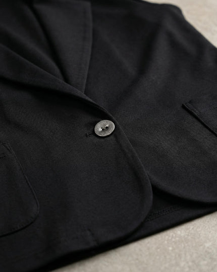 Κοντινή λεπτομέρεια από μαύρο γυναικείο σακάκι σετ σε μεγάλα μεγέθη, εστιάζοντας στο κουμπί, τον γιακά και την υφή του υφάσματος.
