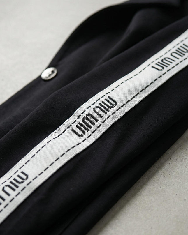 Κοντινή λεπτομέρεια σε μαύρο καθημερινό γυναικείο σετ μεγάλα μεγέθη, που εστιάζει στη λευκή διακοσμητική ρίγα με σχέδιο και στο μεταλλικό κουμπί.