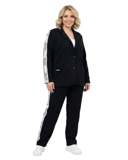 Μαύρο καθημερινό γυναικείο σετ σακάκι και παντελόνι σε μεγάλα μεγέθη, με λευκή διακοσμητική ρίγα στα μανίκια και το πλάι, σε ολόσωμη λήψη.