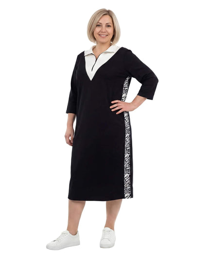 Γυναικείο μαύρο φόρεμα μεγάλα μεγέθη σε σπορ-κομψό στυλ, με λευκό γιακά, φερμουάρ και διακοσμητικές πλαϊνές ρίγες, σε ολόσωμη φωτογραφία.