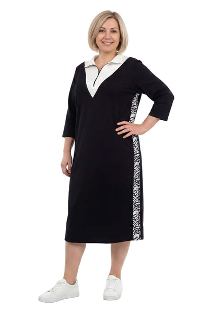 Γυναικείο μαύρο φόρεμα μεγάλα μεγέθη σε σπορ-κομψό στυλ, με λευκό γιακά, φερμουάρ και διακοσμητικές πλαϊνές ρίγες, σε ολόσωμη φωτογραφία.