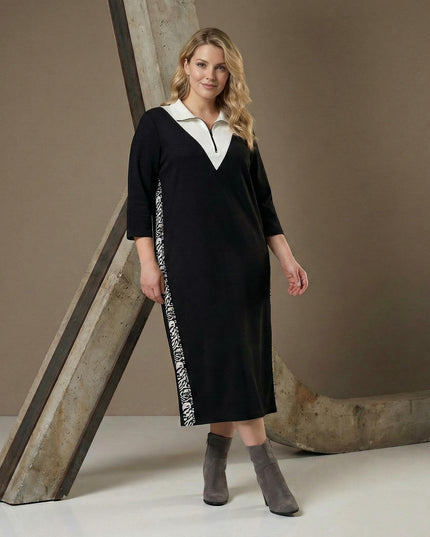 Μαύρο σπορ κομψό φόρεμα σε μεγάλα μεγέθη με λευκό γιακά, φερμουάρ στο ντεκολτέ και πλαϊνές ρίγες, σε ολόσωμη λήψη.