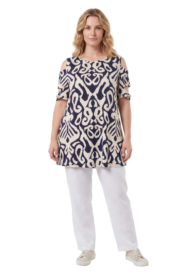 Μπεζ καλοκαιρινή τουνίκ μεγάλα μεγέθη με σκούρο μπλε μοτίβο και ανοιχτούς ώμους. Ολόσωμη λήψη, φορεμένη με λευκό καλοκαιρινό παντελόνι.