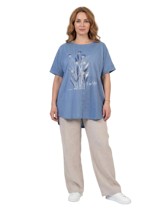 Μπλε καλοκαιρινή τουνίκ μεγάλα μεγέθη με φλοράλ σχέδιο μπροστά. Ολόσωμη λήψη σε λευκό φόντο, φορεμένη με ανοιχτόχρωμο παντελόνι.
