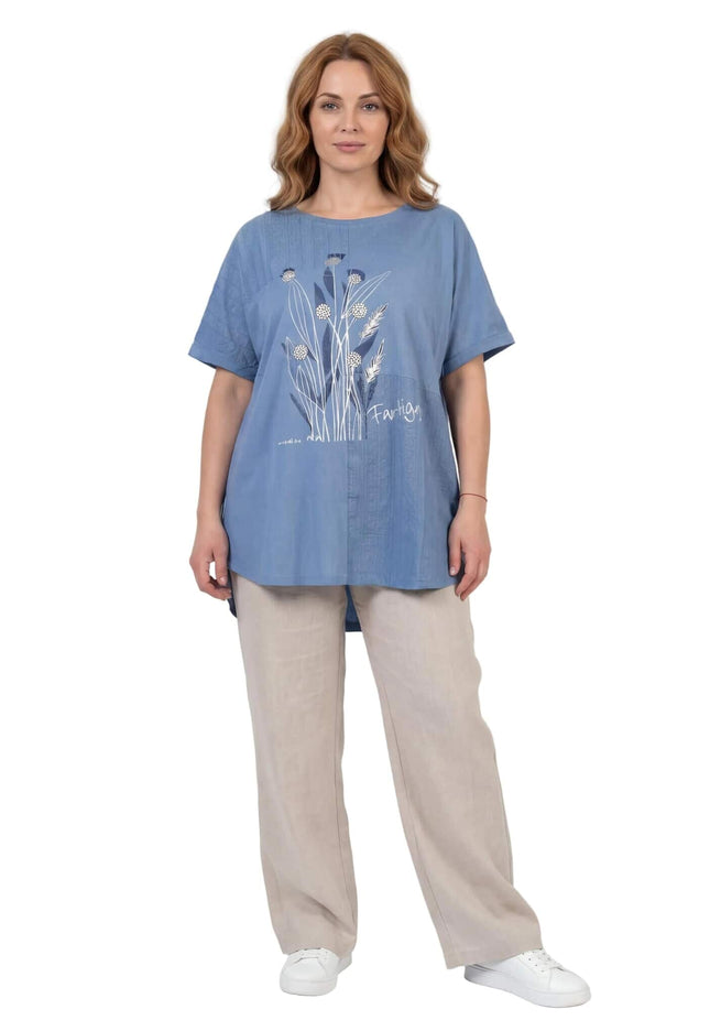 Μπλε καλοκαιρινή τουνίκ μεγάλα μεγέθη με φλοράλ σχέδιο μπροστά. Ολόσωμη λήψη σε λευκό φόντο, φορεμένη με ανοιχτόχρωμο παντελόνι.