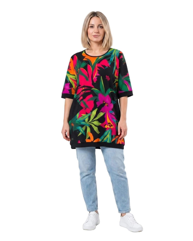 Πολύχρωμη καλοκαιρινή τουνίκ σε μεγάλα μεγέθη με μεγάλο τροπικό φλοράλ σχέδιο. Ολόσωμη λήψη του ρούχου φορεμένου από μοντέλο με τζιν παντελόνι.