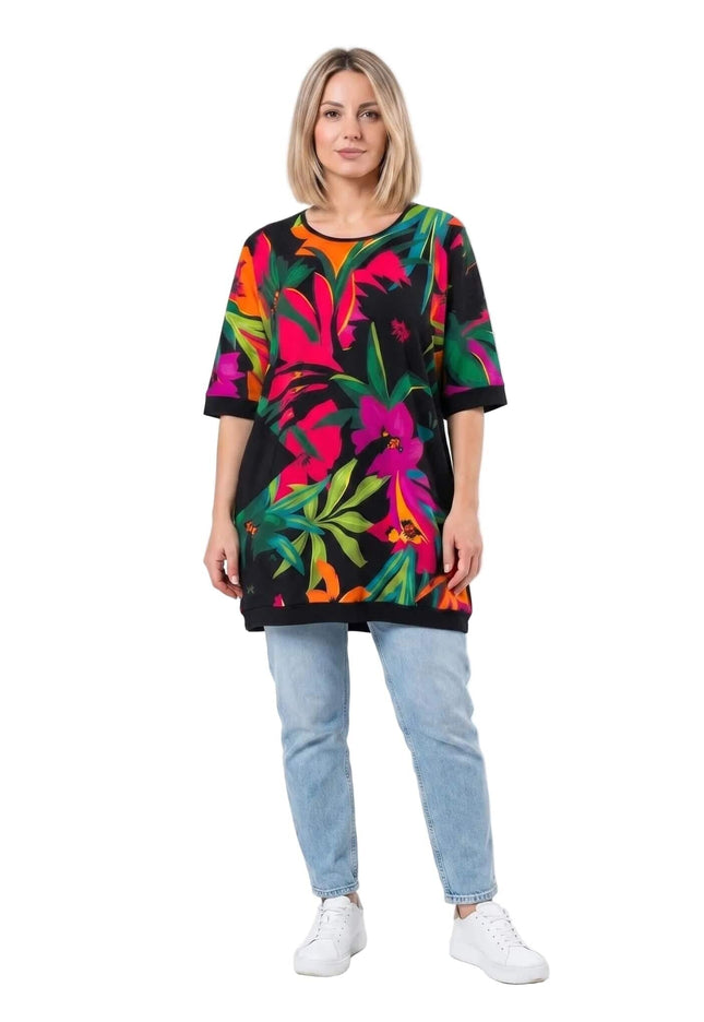 Πολύχρωμη καλοκαιρινή τουνίκ σε μεγάλα μεγέθη με μεγάλο τροπικό φλοράλ σχέδιο. Ολόσωμη λήψη του ρούχου φορεμένου από μοντέλο με τζιν παντελόνι.