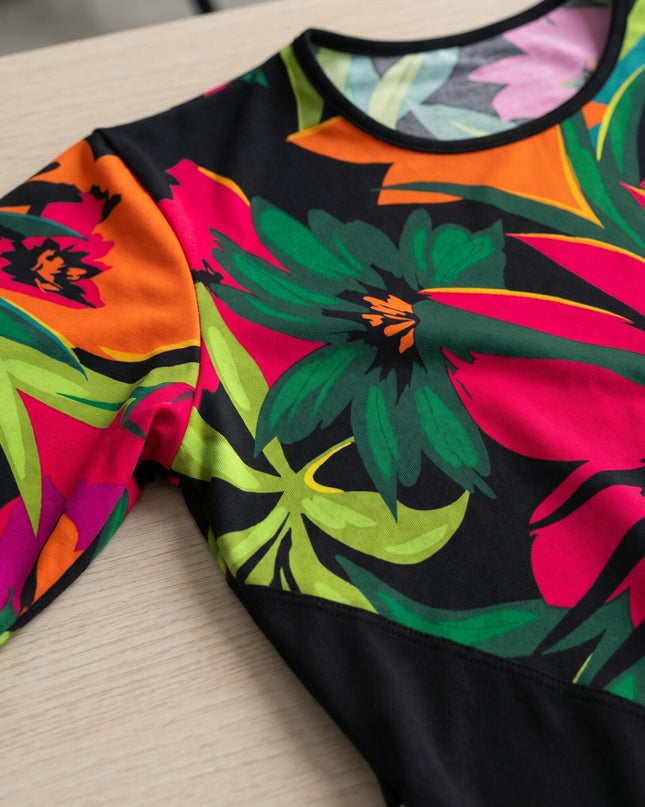 Κοντινή λεπτομέρεια της λαιμόκοψης σε πολύχρωμη τουνίκ για μεγάλα μεγέθη. Διακρίνεται το μαύρο ρέλι και το έντονο τροπικό φλοράλ σχέδιο πάνω στο τραπέζι.