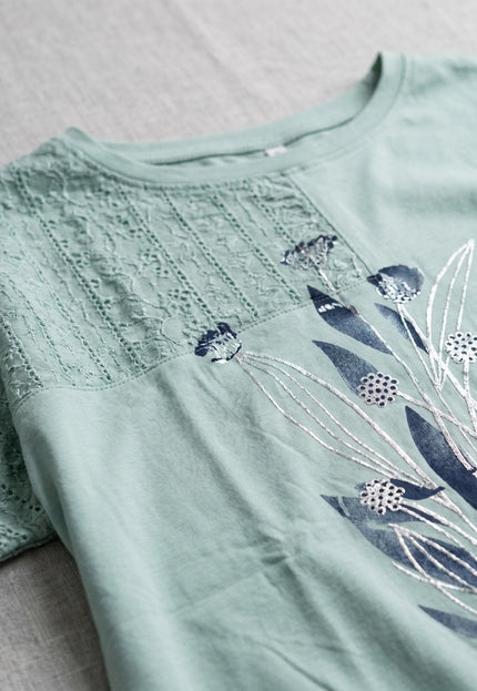 Κοντινή λεπτομέρεια από την πράσινη βαμβακερή τουνίκ σε μεγάλα μεγέθη. Διακρίνονται η λεπτή δαντέλα στους ώμους και το εντυπωσιακό φλοράλ σχέδιο.