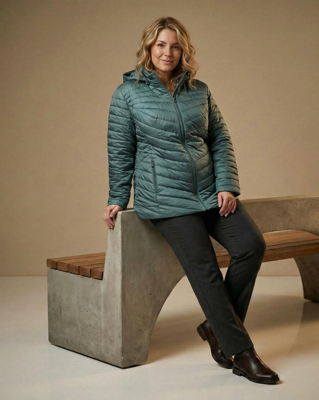 Πράσινο γυναικείο μπουφάν plus size με εβαζέ γραμμή και καπιτονέ σχέδιο, φορεμένο από μοντέλο που ακουμπά σε τσιμεντένιο παγκάκι.