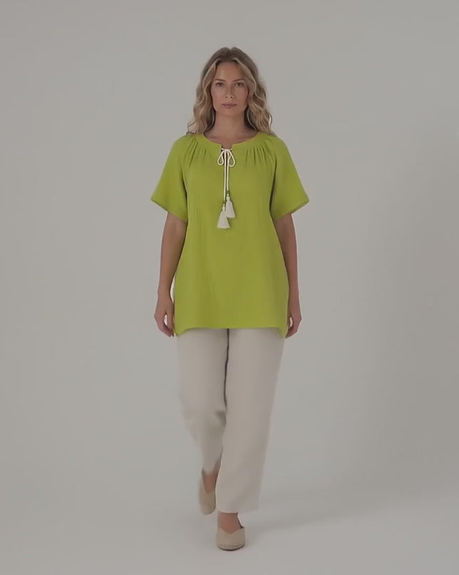 Ένα plus size μοντέλο περπατάει αργά προς την κάμερα σε περιβάλλον στούντιο με ουδέτερο φόντο φορώντας το προϊόν Πράσινη βαμβακερή τουνίκ σε άνετη γραμμή μεγάλα μεγέθη