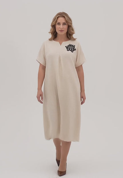 Ένα γυναικείο μοντέλο plus size σε περιβάλλον στούντιο με ουδέτερο φόντο περπατάει αργά προς την κάμερα φορώντας το προϊόν Επίσημο μίντι φόρεμα με φλοράλ απλικέ μπεζ μεγάλα μεγέθη