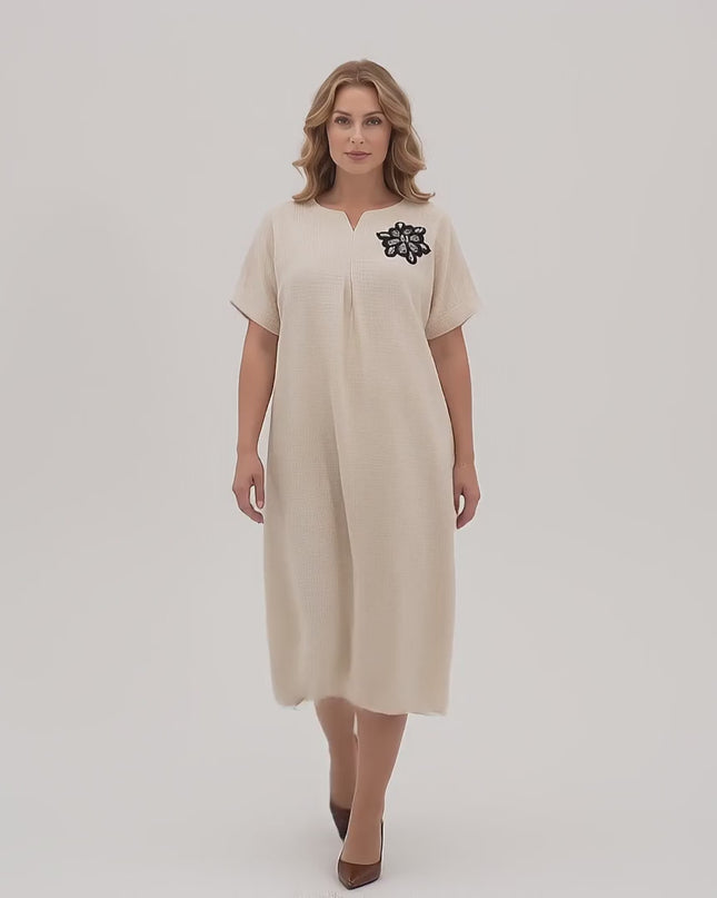Ένα γυναικείο μοντέλο plus size σε περιβάλλον στούντιο με ουδέτερο φόντο περπατάει αργά προς την κάμερα φορώντας το προϊόν Επίσημο μίντι φόρεμα με φλοράλ απλικέ μπεζ μεγάλα μεγέθη