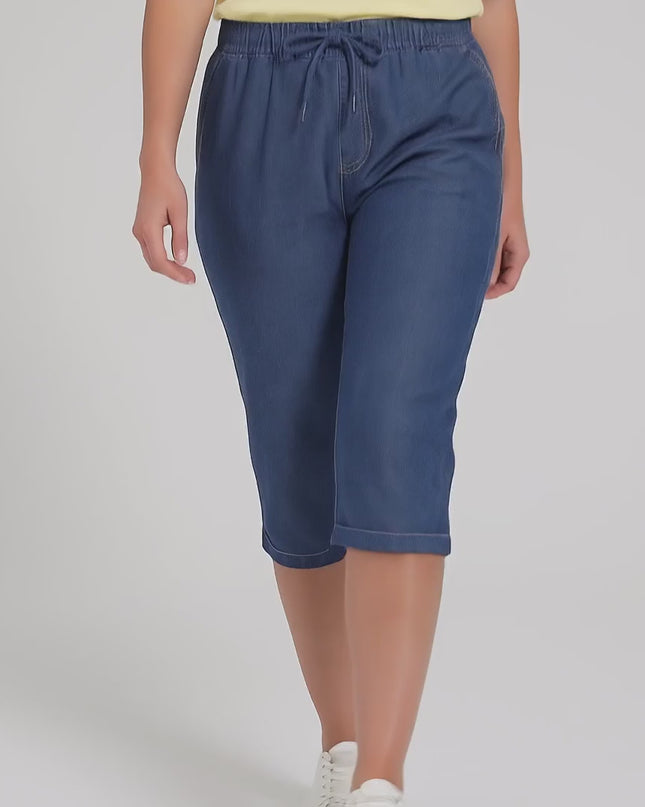 Ένα plus-size μοντέλο σε στούντιο με ουδέτερο φόντο φοράει το Γυναικείο μπλε ελαστικό τζιν παντελόνι 7/8 plus size και περπατάει αργά προς την κάμερα