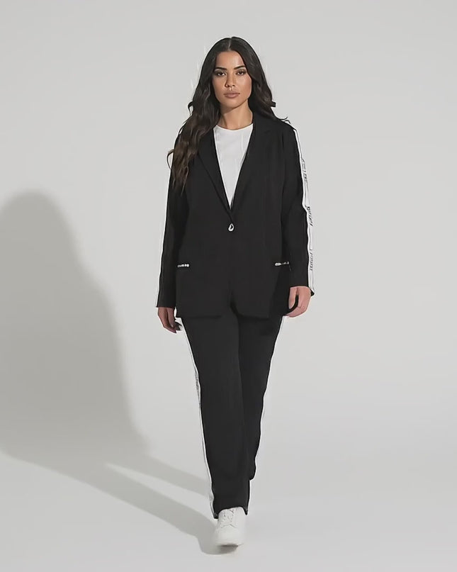 Βίντεο παρουσίασης σε στούντιο με ουδέτερο φόντο όπου ένα plus-size μοντέλο περπατάει αργά προς την κάμερα φορώντας το προϊόν Μαύρο καθημερινό γυναικείο σετ σακάκι και παντελόνι σε μεγάλα μεγέθη