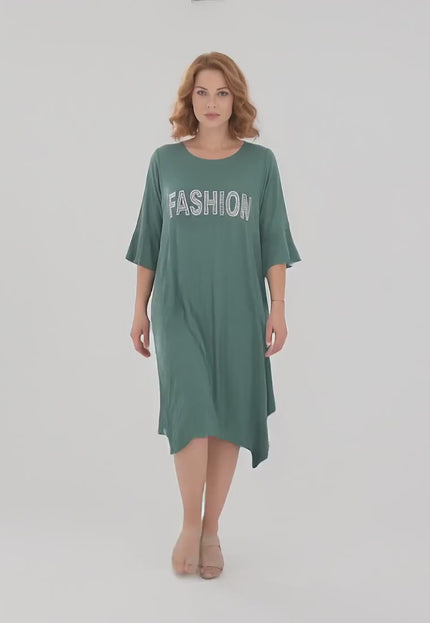 Ένα γυναικείο plus size μοντέλο περπατάει αργά προς την κάμερα σε περιβάλλον στούντιο με ουδέτερο φόντο φορώντας το προϊόν Καθημερινό πράσινο midi φόρεμα μεγάλα μεγέθη με ασύμμετρο τελείωμα