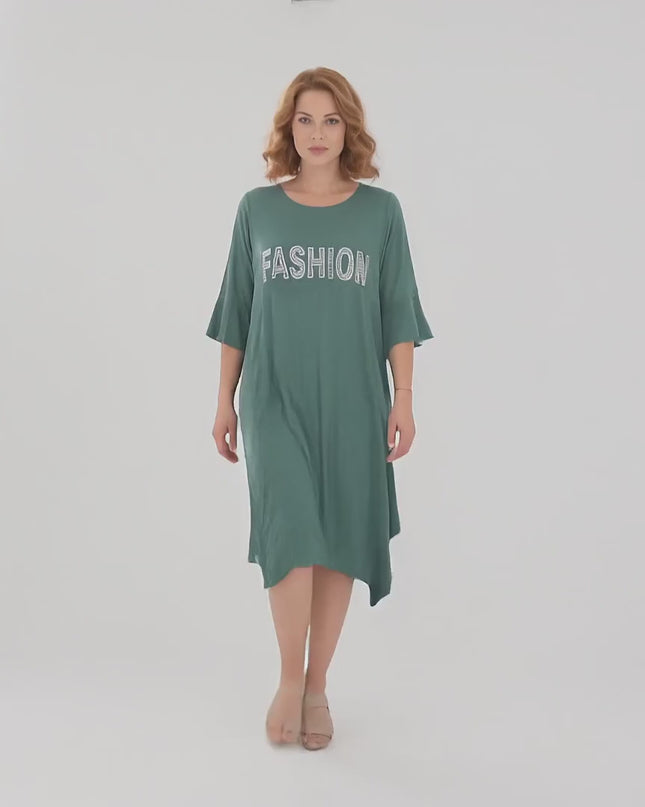 Ένα γυναικείο plus size μοντέλο περπατάει αργά προς την κάμερα σε περιβάλλον στούντιο με ουδέτερο φόντο φορώντας το προϊόν Καθημερινό πράσινο midi φόρεμα μεγάλα μεγέθη με ασύμμετρο τελείωμα