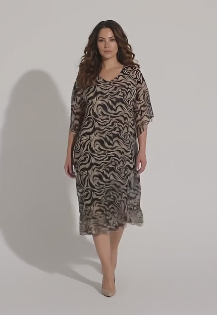 Ένα γυναικείο μοντέλο plus-size περπατάει αργά προς την κάμερα σε περιβάλλον στούντιο με ουδέτερο φόντο φορώντας το Επίσημο μαύρο φόρεμα από σιφόν σε μεγάλα μεγέθη με άνετη γραμμή