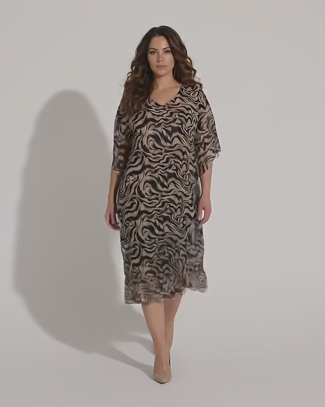 Ένα γυναικείο μοντέλο plus-size περπατάει αργά προς την κάμερα σε περιβάλλον στούντιο με ουδέτερο φόντο φορώντας το Επίσημο μαύρο φόρεμα από σιφόν σε μεγάλα μεγέθη με άνετη γραμμή