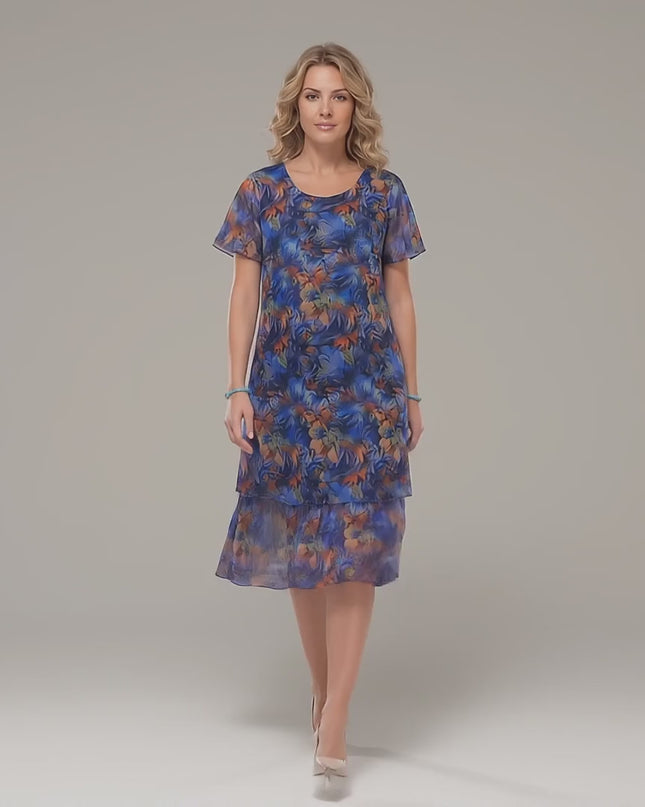 Ένα plus size μοντέλο περπατάει αργά προς την κάμερα σε ένα στούντιο με ουδέτερο φόντο φορώντας το Επίσημο εβαζέ μάξι φόρεμα μεγάλα μεγέθη από πολύχρωμο σιφόν