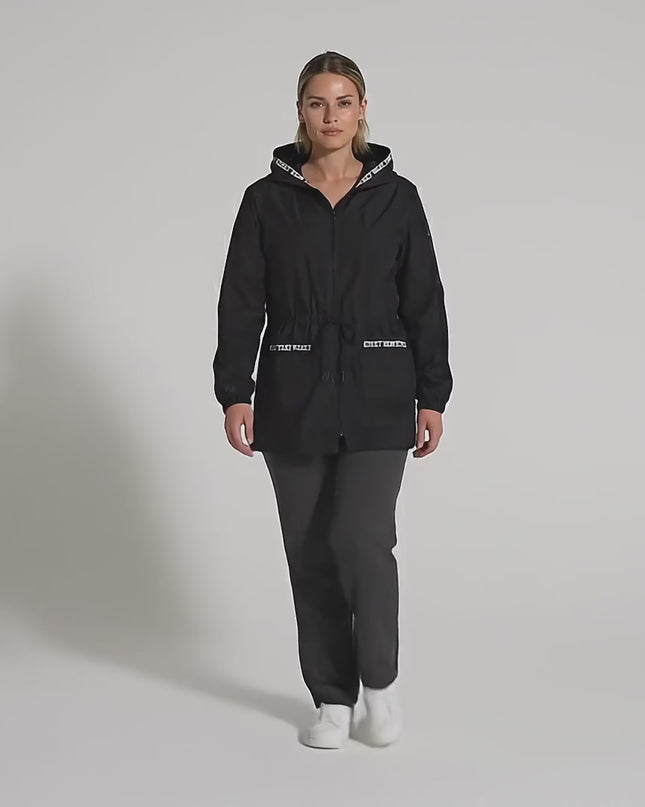 Ένα γυναικείο plus-size μοντέλο περπατάει αργά προς την κάμερα σε περιβάλλον στούντιο με ουδέτερο φόντο, φορώντας Μαύρη ζακέτα σε άνετη γραμμή με κουκούλα και τσέπες