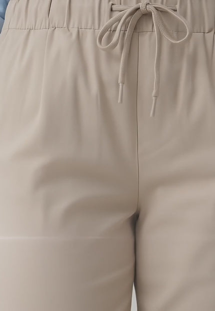 Ένα plus-size μοντέλο περπατά αργά προς την κάμερα σε περιβάλλον στούντιο με ουδέτερο φόντο φορώντας το προϊόν Γυναικείο ελαστικό παντελόνι μεγάλα μεγέθη σε μπεζ χρώμα