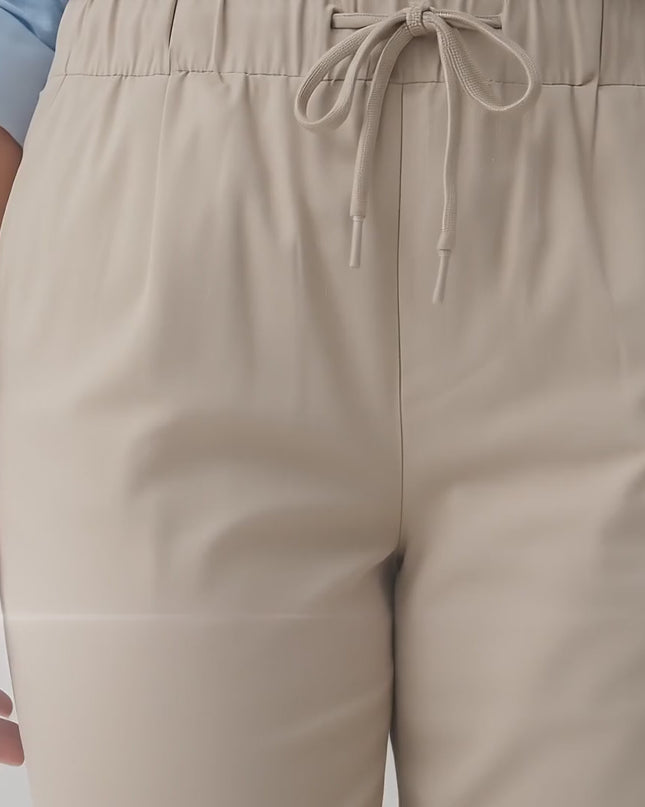 Ένα plus-size μοντέλο περπατά αργά προς την κάμερα σε περιβάλλον στούντιο με ουδέτερο φόντο φορώντας το προϊόν Γυναικείο ελαστικό παντελόνι μεγάλα μεγέθη σε μπεζ χρώμα