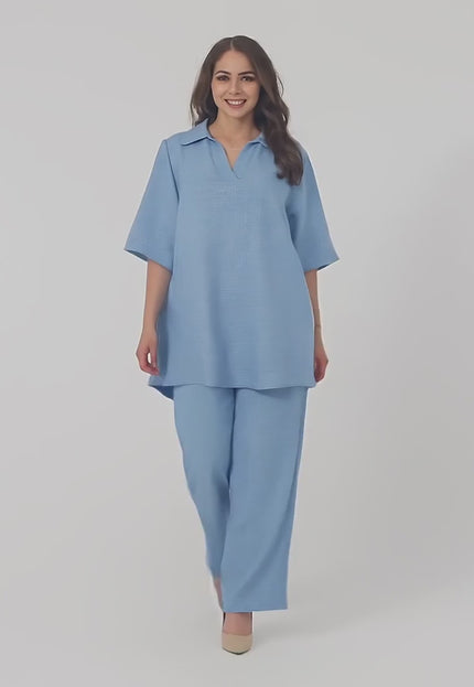 Ένα plus-size μοντέλο φοράει το Σετ με τουνίκ και παντελόνι σε μεγάλα μεγέθη και περπατάει αργά προς την κάμερα σε περιβάλλον στούντιο με ουδέτερο φόντο