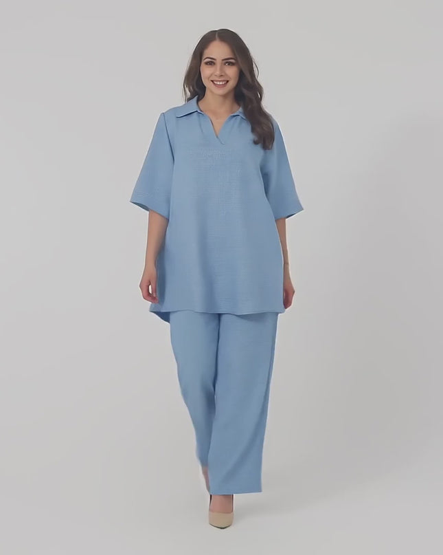 Ένα plus-size μοντέλο φοράει το Σετ με τουνίκ και παντελόνι σε μεγάλα μεγέθη και περπατάει αργά προς την κάμερα σε περιβάλλον στούντιο με ουδέτερο φόντο