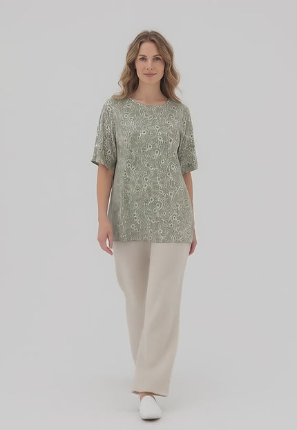 Ένα plus-size μοντέλο περπατάει αργά προς την κάμερα σε περιβάλλον στούντιο με ουδέτερο φόντο, φορώντας το προϊόν Γυναικεία καθημερινή φλοράλ τουνίκ με άνοιγμα στους ώμους