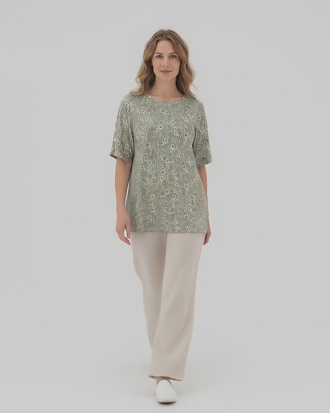 Ένα plus-size μοντέλο περπατάει αργά προς την κάμερα σε περιβάλλον στούντιο με ουδέτερο φόντο, φορώντας το προϊόν Γυναικεία καθημερινή φλοράλ τουνίκ με άνοιγμα στους ώμους