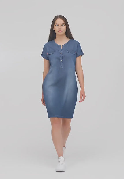 Ένα plus-size μοντέλο περπατάει αργά προς την κάμερα σε περιβάλλον στούντιο φορώντας το Φόρεμα Τζιν- Σκούρο Μπλε - V-λαιμόκοψη - Κουμπιά- Άνοιξη-Καλοκαίρι
