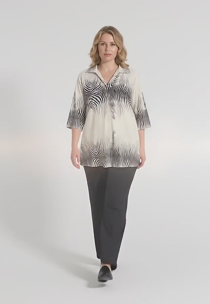 Ένα plus size γυναικείο μοντέλο περπατάει αργά προς την κάμερα μέσα σε περιβάλλον στούντιο φορώντας το Επίσημο μπεζ πουκάμισο σε μεγάλα μεγέθη με V και κοντό μανίκι