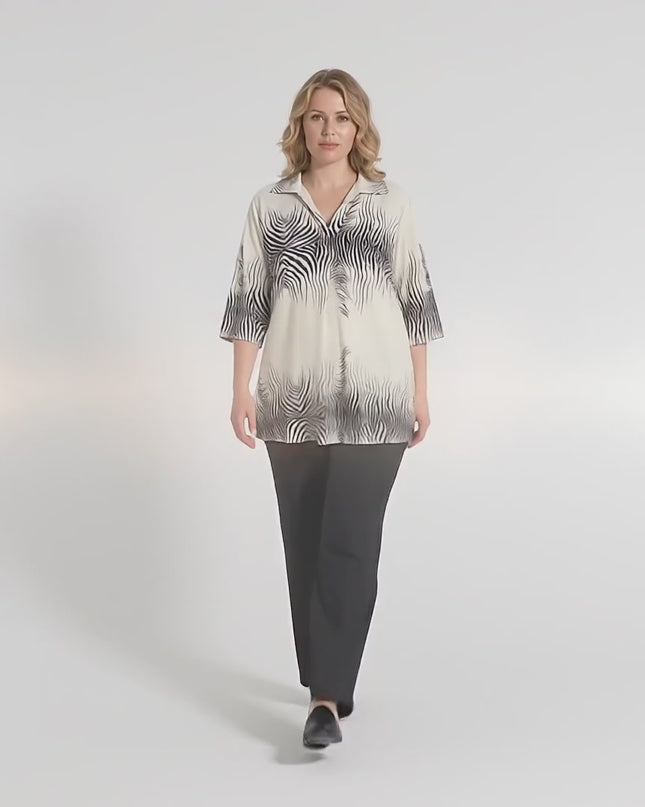 Ένα plus size γυναικείο μοντέλο περπατάει αργά προς την κάμερα μέσα σε περιβάλλον στούντιο φορώντας το Επίσημο μπεζ πουκάμισο σε μεγάλα μεγέθη με V και κοντό μανίκι