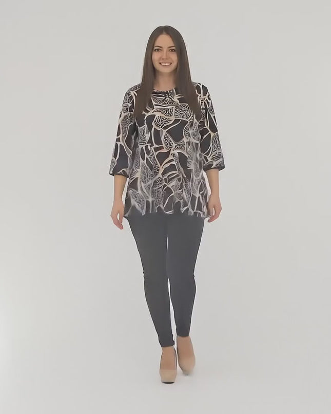 Βίντεο παρουσίασης σε περιβάλλον στούντιο με ουδέτερο φόντο όπου ένα plus-size γυναικείο μοντέλο περπατάει αργά προς την κάμερα φορώντας το προϊόν Φαρδιά τουνίκ με αφηρημένο σχέδιο και φιόγκο