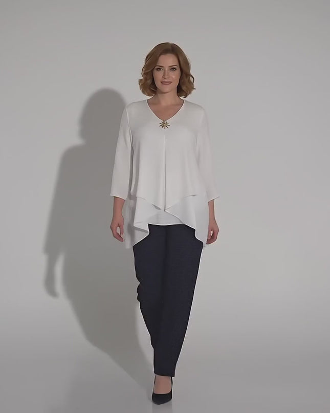 Βίντεο παρουσίασης σε περιβάλλον στούντιο με ουδέτερο φόντο όπου ένα plus size μοντέλο περπατάει αργά προς την κάμερα και φοράει το προϊόν Επίσημη λευκή τουνίκ μεγάλα μεγέθη με ασύμμετρη γραμμή και καρφίτσα