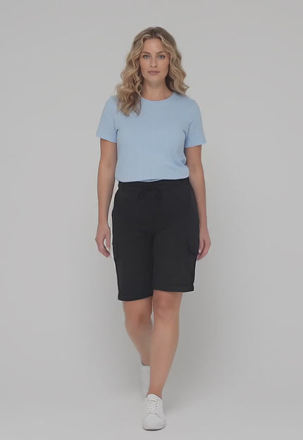 Ένα plus size μοντέλο περπατάει αργά προς την κάμερα σε περιβάλλον στούντιο με ουδέτερο φόντο φορώντας το προϊόν Γυναικείο μαύρο λινό σορτς σε ίσια γραμμή