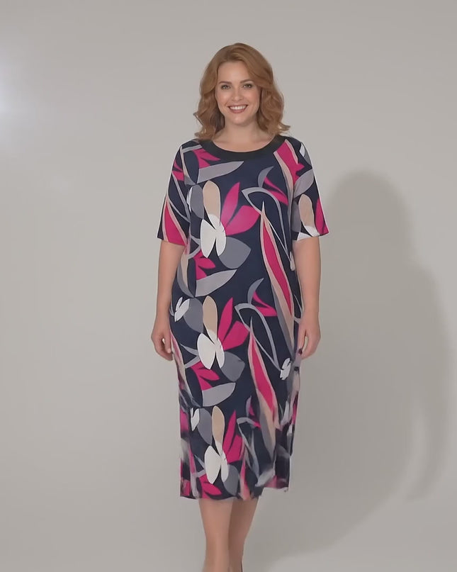 Ένα plus-size μοντέλο περπατάει αργά προς την κάμερα σε περιβάλλον στούντιο με ουδέτερο φόντο φορώντας το Επίσημο σκούρο μπλε φλοράλ μάξι φόρεμα σε γραμμή Α