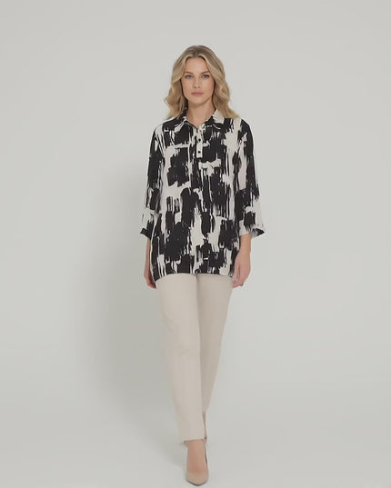 Ένα plus-size μοντέλο σε περιβάλλον στούντιο με ουδέτερο φόντο περπατά αργά προς την κάμερα φορώντας το προϊόν Елегантна официална макси риза в черно и бяло със свободен силует