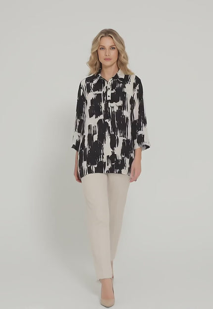 Ένα plus-size μοντέλο σε περιβάλλον στούντιο με ουδέτερο φόντο περπατά αργά προς την κάμερα φορώντας το προϊόν Елегантна официална макси риза в черно и бяло със свободен силует