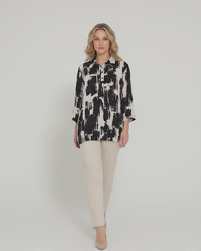 Ένα plus-size μοντέλο σε περιβάλλον στούντιο με ουδέτερο φόντο περπατά αργά προς την κάμερα φορώντας το προϊόν Елегантна официална макси риза в черно и бяло със свободен силует