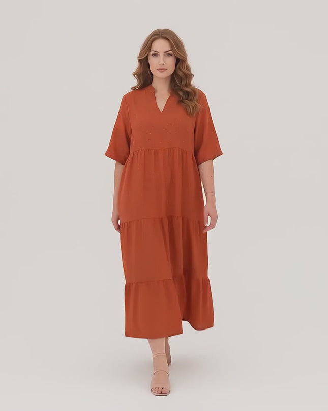 Ένα plus-size γυναικείο μοντέλο σε περιβάλλον στούντιο με ουδέτερο φόντο περπατάει αργά προς την κάμερα φορώντας το Επίσημο Μάξι Φόρεμα Κεραμιδί σε Μεγάλα Μεγέθη